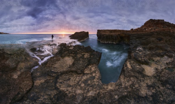 Captivating sunrise over rocky shoreline at Cabo Cervera in Torrevieja, Alicante, Spain A lone figure stands against the vibrant sky, surrounded by serene sea waves