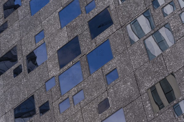 Detailed view of a modern building facade showcasing varying window sizes and a textured exterior surface under clear skies