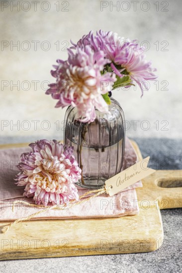 Elegant chrysanthemums in a textured glass vase, set on a wooden board, create an autumnal theme A handwritten Autumn tag adds a charming touch to this serene display