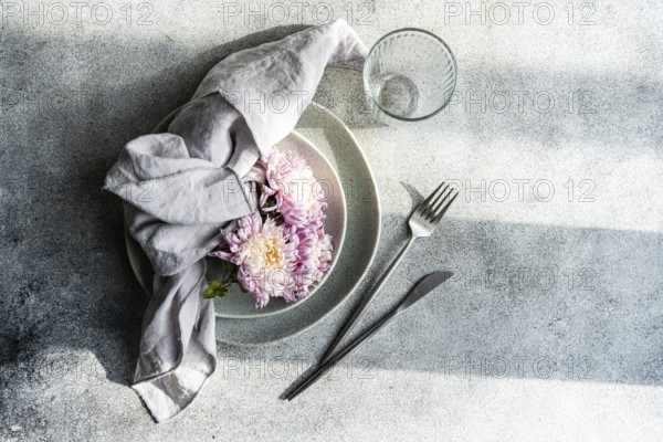 An elegant table setting featuring pink chrysanthemums on a grey plate, accompanied by a linen napkin and stainless steel cutlery, creating a serene autumnal ambiance