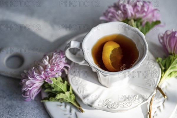 Elegant autumn-themed setup featuring a hot beverage with a lemon slice in a white cup Surrounded by delicate pink chrysanthemums on a rustic surface