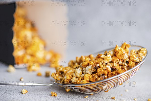 Gourmet sweet caramel popcorn in a shiny wire basket, the sugary golden pieces bathed in caramel sit temptingly against a neutral grey background