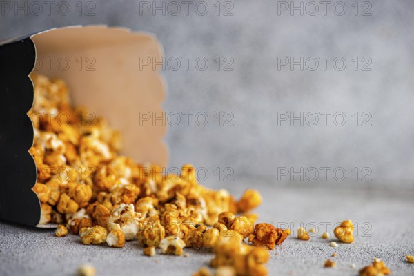 Caramel popcorn tumbling out of a black carton onto a textured gray background