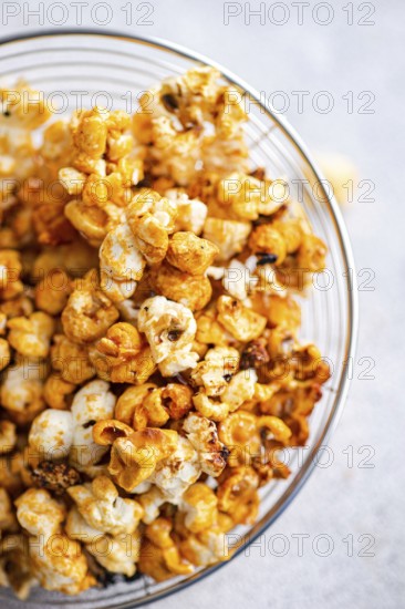 Top view of a glass bowl overflowing with caramel-coated popcorn, showcasing a mix of golden hues and crunchy textures