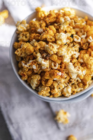 Top view of a bowl filled with crunchy caramel popcorn on a textured cloth background