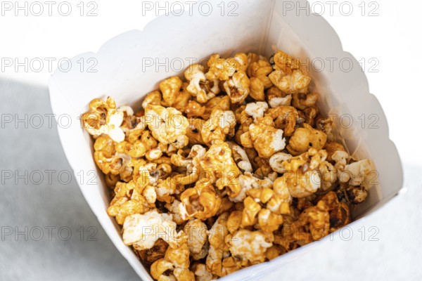 Top view of delicious caramel-coated popcorn filling a white paper container, showcasing a range of golden to deep brown hues