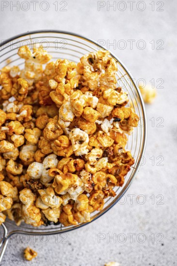 Top view of a glass bowl overflowing with crunchy caramel popcorn, staged on a soft gray background