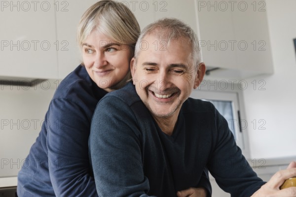 A joyful senior couple shares a tender moment, embracing in their modern kitchen The scene captures warmth, happiness, and the enduring bond of a loving relationship