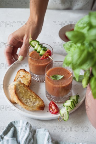 A refreshing summer meal with chilled gazpacho garnished with cucumber, tomato, and basil, accompanied by crispy toasted bread, set on a white plate