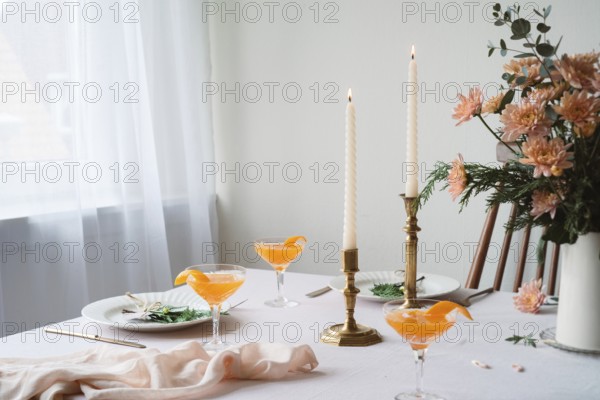 An elegantly set table featuring refreshing Mandarin drinks, lit beeswax candles, intricate floral arrangements, and fine dining utensils. A serene, sophisticated ambiance perfect for a special occasion