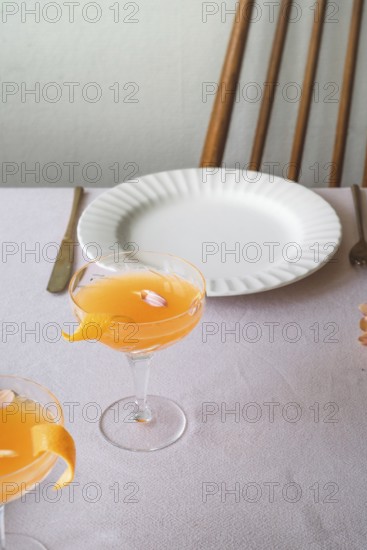 A well-appointed dining table featuring a bright mandarin drink in a sophisticated glass, complemented by a classic white plate and vintage cutlery on a textured tablecloth