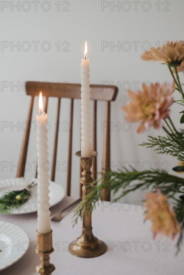 A serene dinner table setup featuring two lit taper candles in brass holders, complemented by fresh flower decor and subtle tableware, ideal for a sophisticated dining atmosphere