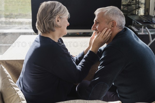 An intimate moment between a senior couple, sitting closely and smiling at each other The warmth and affection between them create a cozy, loving atmosphere