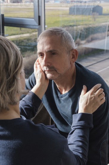 A senior couple shares a tender moment near a sunlit window, with one gently holding the other's face This intimate scene captures love, warmth, and companionship in later years