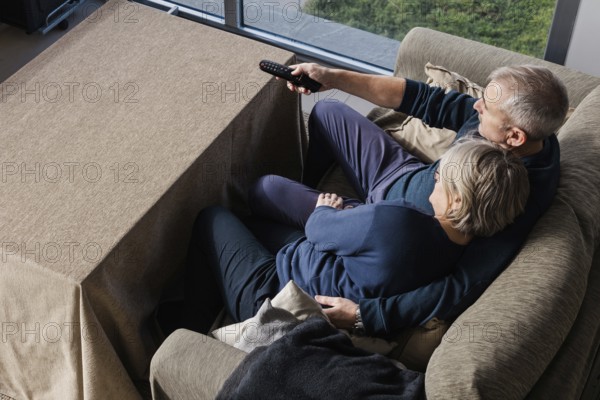 A senior couple sits closely on a comfortable couch, sharing a peaceful moment watching TV together, highlighting warmth, connection, and companionship at home