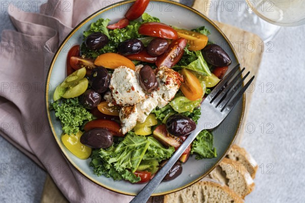 Top view of a nutritious salad featuring raw Kale leaves, multi-colored cherry tomatoes, sliced red onions, BBQ-flavored olives, and spiced feta cheese drizzled with olive oil, served on a stylish plate