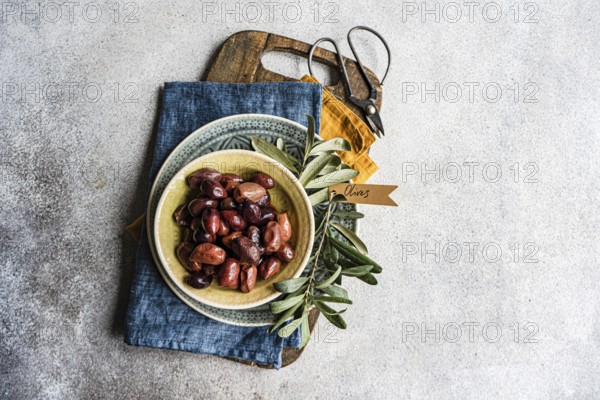 Top view of a rustic-styled bowl filled with Greek BBQ olives on a wooden cutting board with fresh olive branches, ideal for a Mediterranean-themed culinary setting