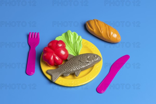 A colorful display with plastic toy food on a plate, including fish, bread, and vegetables, critiquing modern diet culture and the prevalence of junk food
