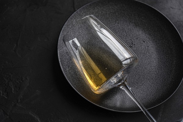 From above, an elegant glass of dry white wine placed carefully on a textured black plate, reflecting sophistication and calmness against a stark, dark background