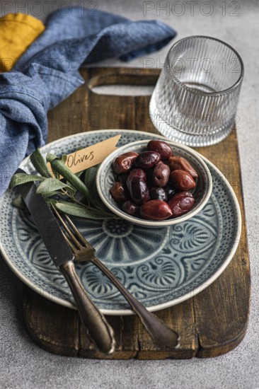 A tasteful arrangement of Greek BBQ olives on a ceramic plate, accompanied by a glass, rustic utensils, and textured linens. The scene captures a balance of elegance and tradition, perfect for culinary themes