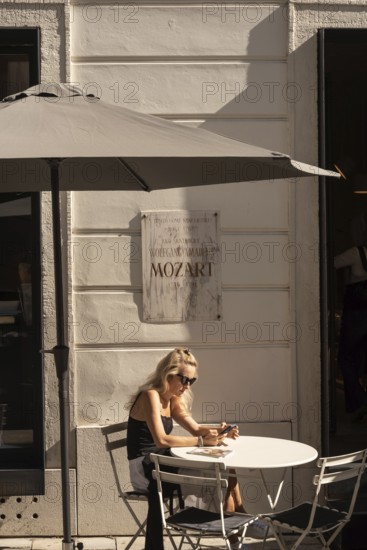 Bratislava, Slovakia. October 2nd 2023 A Woman sits at a Cafe beside a memorial Plaque outside the Pallfys Palace, where Wolfgang Amadeus Mozart gave a concert in Bratislava in 1762, at aged 6