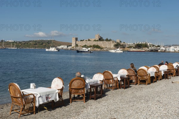 Bodrum, Mugla, Turkey. April 21st 2022 Restaurant Tables on the beach in Bodrum harbour with Bodrum Castle in the background, the Aegean coast of south west Turkey
