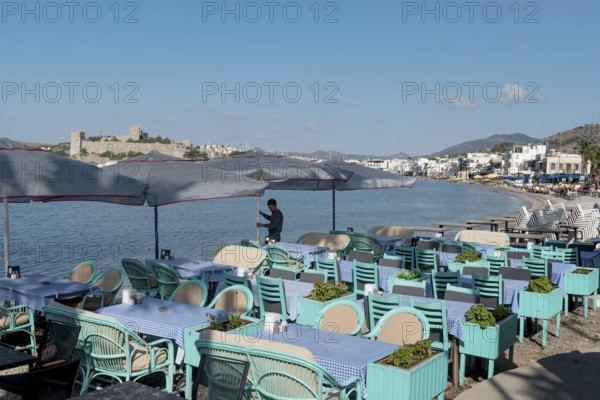 Bodrum, Mugla, Turkey. April 21st 2022 A waiter prepares tables on the beach side cafe in Bodrum harbour with Bodrum Castle in the background, the Aegean coast of south west Turkey