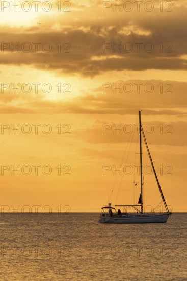 A serene view of a sailboat gliding across calm waters at sunset, surrounded by golden skies, captured near La Zenia, Cabo Roig, Orihuela Costa, Alicante, Spain