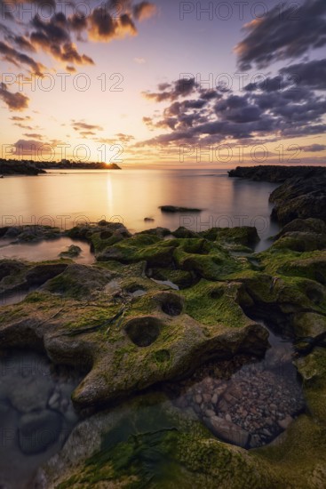 Stunning sunset over the rocky coast of Cabo Roig, Orihuela, Alicante, Spain The sky's warm hues reflect on the water, creating a tranquil and picturesque scene