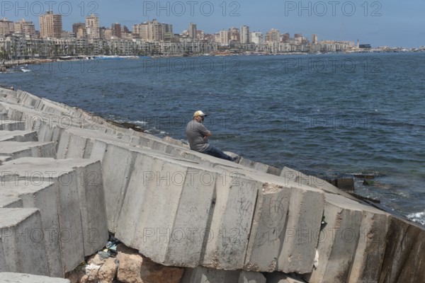 A man sits alone on the concrete breakwater, a barrier for potential flooding, the Egyptian Mediterranean city is at risk of rising sea levels, Egypt