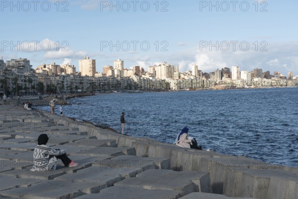 Alexandria, Egypt. December 1st 2022 Egyptian people on concrete blocks positioned as a defence against rising Mediterranean sea levels along the Corniche of Alexandria, the seconds largest city in Egypt