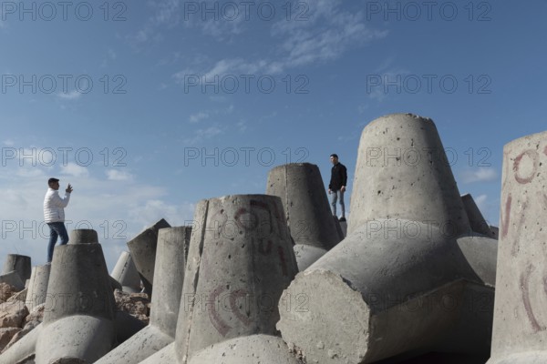 Alexandria, Egypt. December 1st 2022 Young Egyptian men take photographs on massive concrete blocks designed to protect the Mediterranean Sea front of Alexandria, Egypt