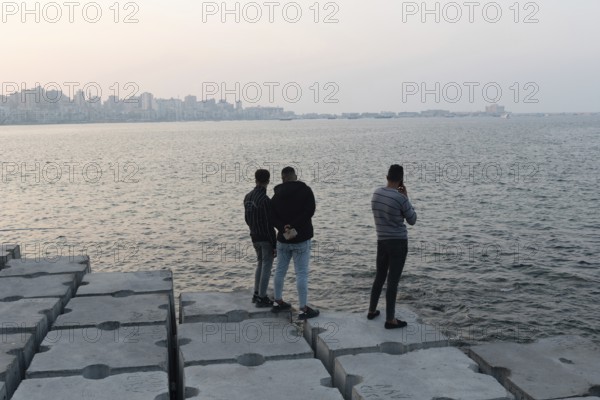 Alexandria, Egypt. December 1st 2022 Young Egyptian men standing on large concrete blocks designed to protect the Mediterranean coastal city of Alexandria, Egypt