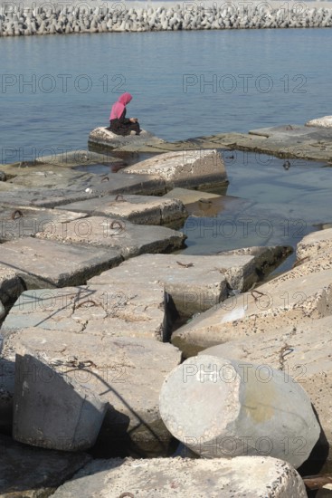 Alexandria, Egypt. December 1st 2022 Muslim women wearing a pink hijab sitting on large concrete slabs designed to protect the Mediterranean coastal city of Alexandria, Egypt