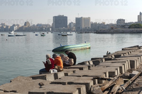 Alexandria, Egypt. December 1st 2022 People on concrete blocks positioned as a defence against rising sea levels along the Corniche of Alexandria, the seconds largest city in Egypt