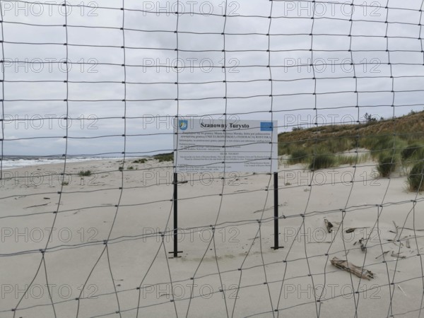 Border between Poland and the Russian exclave of Kaliningrad on the fresh spit in Poland, secluded beach with sand dunes, sea and a fence under a cloudy sky, Poland