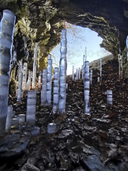 Icicles rise in a brightly lit rock cave with colorful leaves, hiking in the Franconian Forest nature park Park