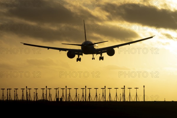 Boeing 777 commercial passenger jet aircraft in flight on approach to land over runway lights silhouette at sunset at London Stansted airport, Essex, England, United Kingdom
