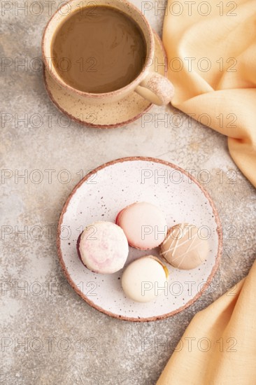 Macarons colourful cookies dessert, cup of coffee, on brown concrete background with orange linen textile, close up, top view, flat lay