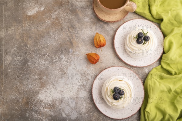 Pavlova Meringue dessert with crisp meringue and blueberry, cup of coffee, on brown concrete background with green linen textile, copy space, top view, flat lay