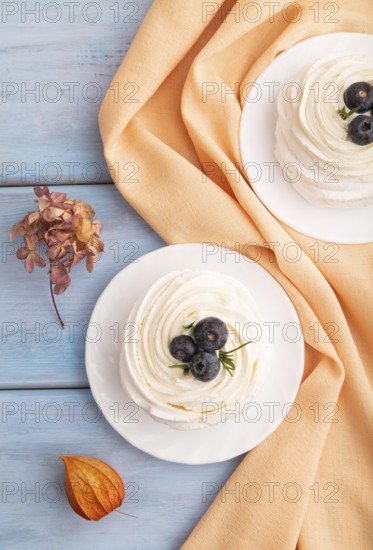 Pavlova Meringue dessert with crisp meringue and blueberry on blue wooden background with orange linen textile, close up, top view, flat lay