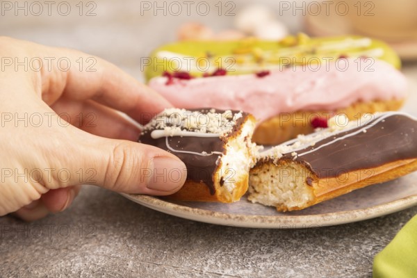 Glazed Eclairs on brown concrete background and green linen textile with hand, cup of coffee, side view, close up, selective focus