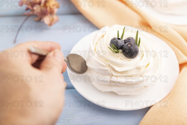 Pavlova Meringue dessert with crisp meringue and blueberry with hand on blue wooden background with orange linen textile, close up, side view, selective focus