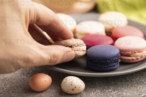 Macarons colourful cookies dessert with hand on brown concrete background with green linen textile, close up, side view, selective focus