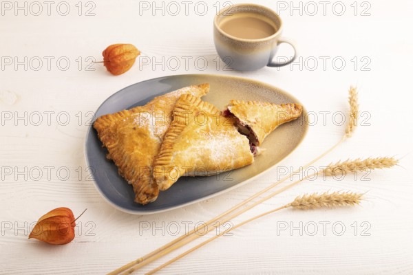 Triangles Pie, Puff Pastry, Samsa with cherry jam on white wooden background, cup of coffee, side view, close up