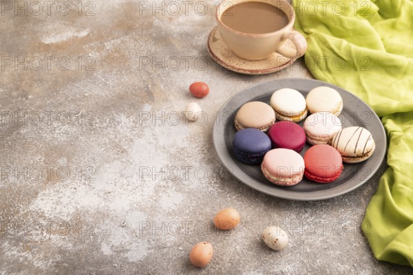 Macarons colourful cookies dessert, cup of coffee, on brown concrete background with green linen textile, copy space, side view