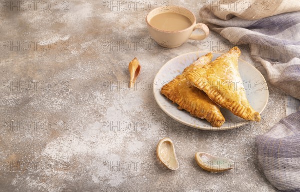 Triangles Pie, Puff Pastry, Samsa with cherry jam on brown concrete background and linen textile, cup of coffee, side view, copy space