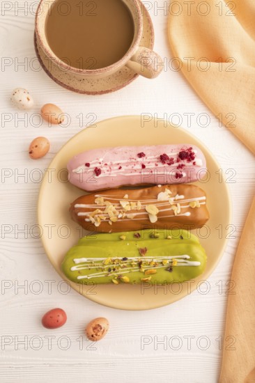 Glazed Eclairs on white wooden background and orange linen textile, cup of coffee, top view, flat lay, close up