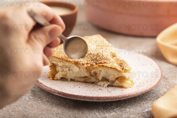 Apple Charlotte cake with hand on brown concrete background and orange linen textile, cup of milk, side view, close up, selective focus