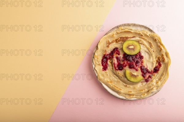 Stack of Plain Fried pancakes with jam and kiwi on pink and orange pastel paper background. top view, flat lay, copy space